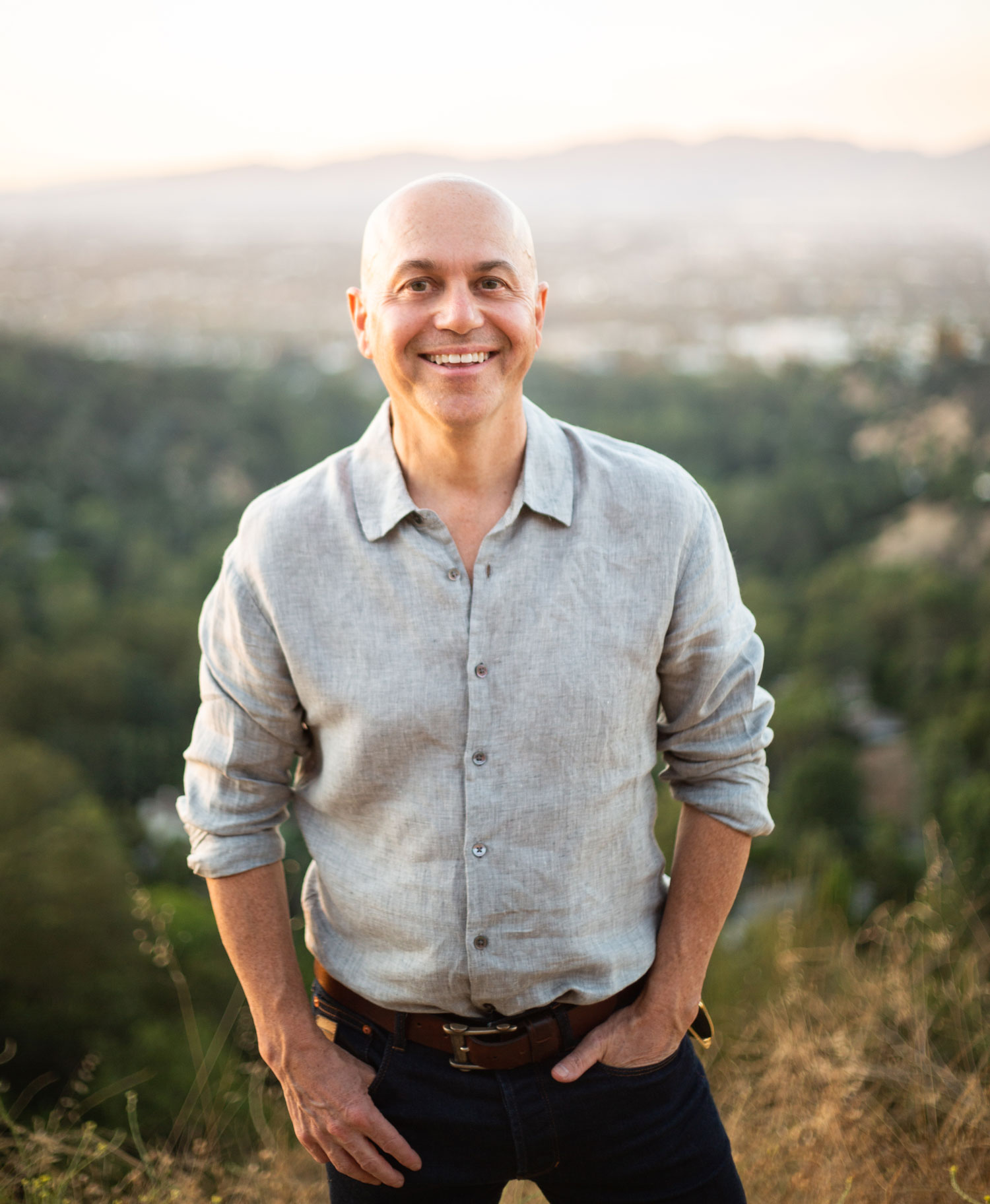 alan watt standing in front of an L.A. Hillside smiling, hand in pocket